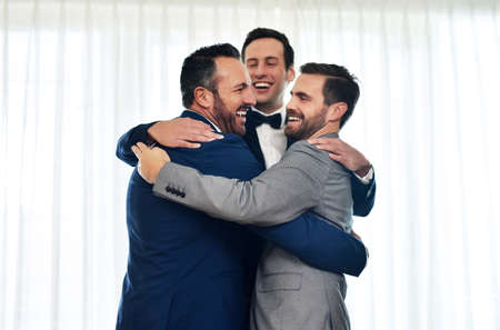 Blessed to have them with me on this special day. Shot of two groomsmen hugging and celebrating with the bridegroom on his wedding way.の写真素材
