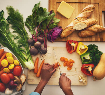 Time to cook. Shot of an unrecognizable persons hands chopping vegetables on a cutting board in the kitchen at home.の写真素材
