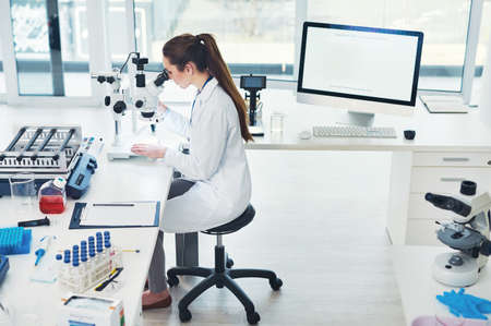So much work still to do. Cropped shot of a focused young female scientist looking through a...