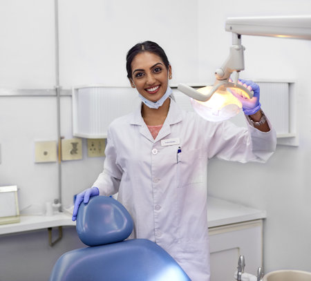 Dont forget to schedule regular checkups with your dentist. Portrait of a young female dentist standing alongside the dental chair in her office.の写真素材