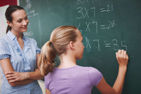Improving on her mathematics. A pretty young teacher helping her student with a maths problem at the blackboard.の写真素材