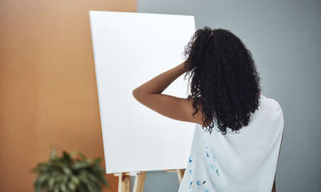 The creative block is real. Rearview shot of a young woman looking frustrated while trying to paint on a canvas at home.の写真素材