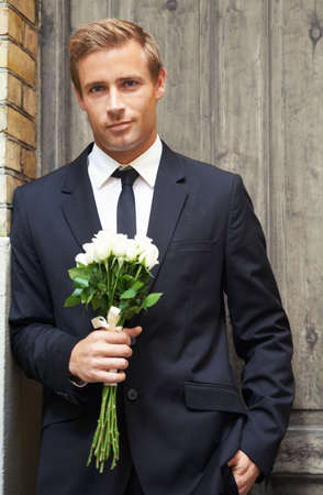 Dream guy. Portrait of a handsome man smiling and holding a bunch of white roses.の写真素材