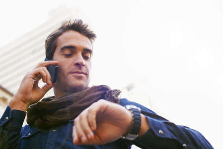 Hes always got some time..... Low angle shot of a man chekcing his watch while talking on his...