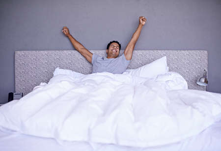 Best nights sleep ever. A young man stretching out while waking.