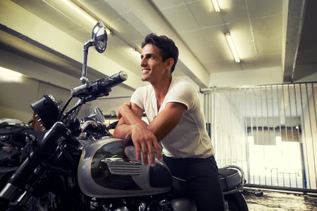 Getting a feel for biking. A handsome young man sitting on his motorcycle.の写真素材