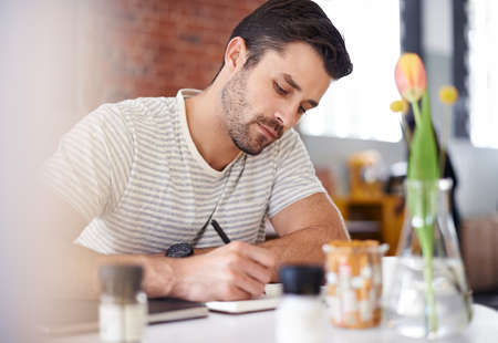 The write stuff. Shot of a handsome young man writing in a notebook while sitting at a restaurant...