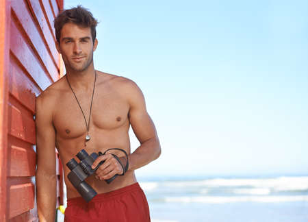 Hes looking out for danger in the water. A handsome young lifeguard at the beach.の写真素材