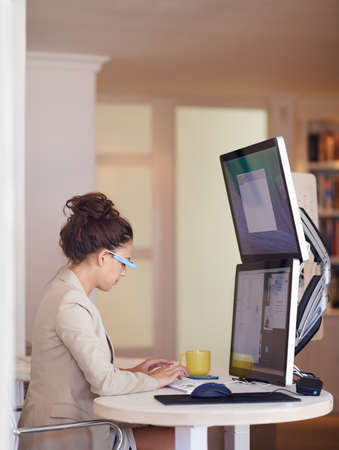 Shot of a young woman wearing smart glasses while working on a dual-screen computer. The commercial...