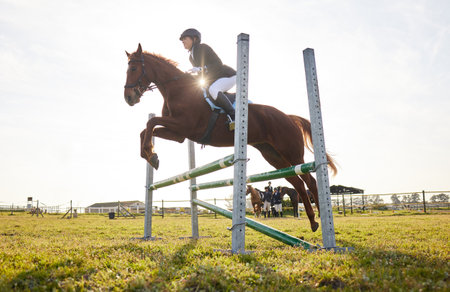 In riding a horse, we borrow freedom. Shot of a young rider jumping over a hurdle on her horse.の写真素材