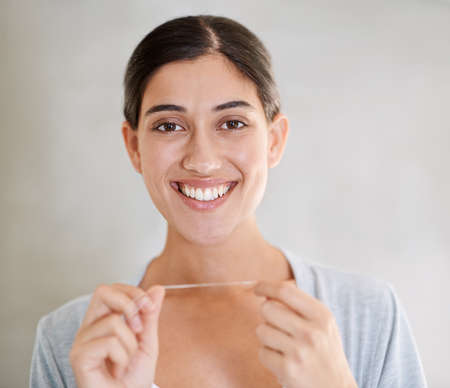 Regular flossing keeps my smile perfect. Portrait of an attractive young woman flossing her teeth.