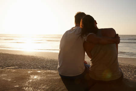 Life is perfect with you by my side. Silhouette of a couple sitting beside each other at the beach.の写真素材