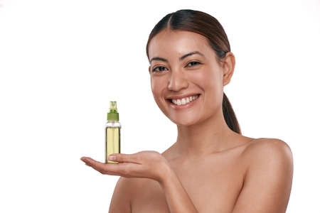 It helps keep your face fresh for longer. Shot of a beautiful young woman holding up a bottle of face mist.の写真素材