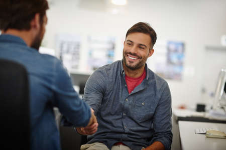 Great doing business with you. Shot of two young businessmen shaking hands together at a desk in an...