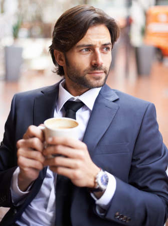 Sitting watching the world go by. A thoughtful businessman drinking coffee outdoors at a coffee shop.の写真素材