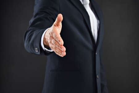 Lets do business. Cropped shot of a businessman extending his arm to shake hands against a black background.の写真素材