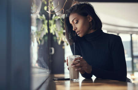 Never keep a good woman waiting. Shot of a beautiful young woman drinking a iced coffee in a cafe.の写真素材