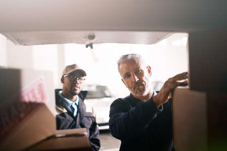 Loading your goods with the utmost care. Shot of delivery men loading boxes into a vehicle.の写真素材