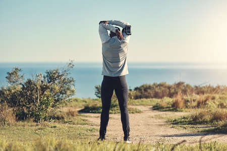 Preparation is key. Rearview shot of an unrecognizable young man stretching before exercising outdoors.の写真素材