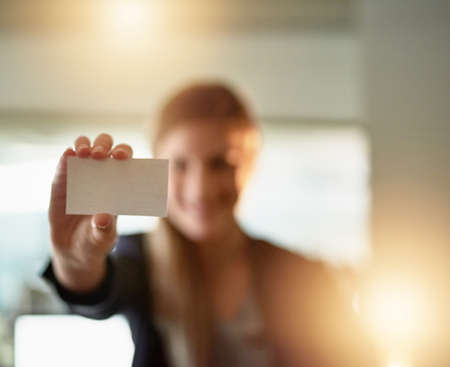Here, take my number. Shot of a young businesswoman holding up a blank businesscard in the office.の写真素材