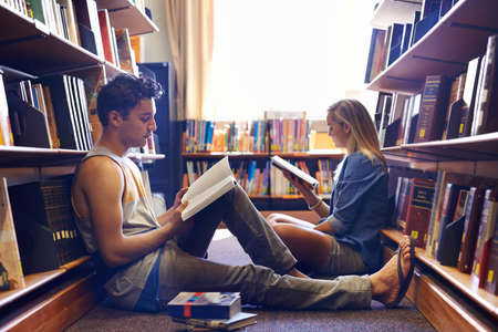 Studying together, but separately. Two students reading separate textbooks in the library.