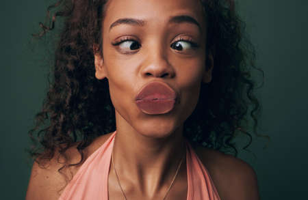 Squishy kisses. Cropped shot of an attractive and quirky young woman posing against a green background in studio.の写真素材