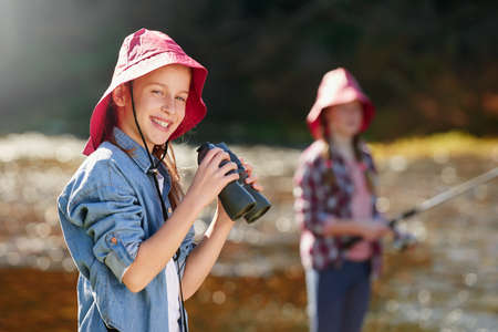 Enjoying a day of adventure along the river. A young girl holding a pair of binoculars in the outdoors.の写真素材