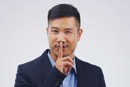 This is what you call a non-disclosure agreement. Portrait of a handsome businessman posing with his finger on his lips against a grey background.の写真素材