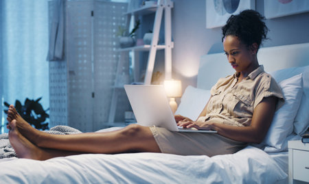Time for some late night blogging. Shot of an attractive young woman using her laptop while lying on her bed after a long day at work.の写真素材