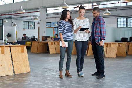 Theyve got technology on their side. Three staff members chatting about something on a digital tablet in their office space.の写真素材