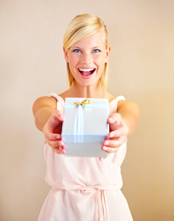 Surprise - its for you. Portrait of a young woman holding out a gift box and smiling.の写真素材