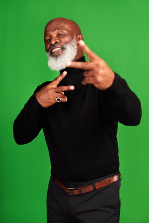 Show me someone cooler than me. Studio shot of a senior man showing peace signs while posing against a green background.の写真素材
