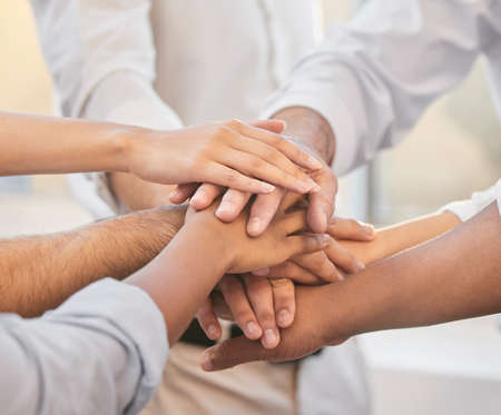 On three. Cropped shot of an unrecognizable group of businesspeople huddled together in the office and piling their hands in the middle.の写真素材