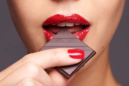 Every woman needs a guilt-free chocolate day. Closeup portrait of a cute young female biting on a chocolate bar.の写真素材