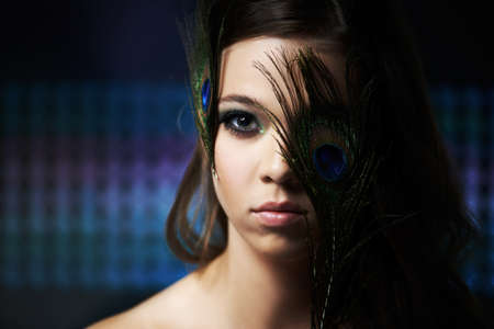 Irridescent beauty. Dramatic portrait of a young woman with her face partially covered by some feathers.の写真素材