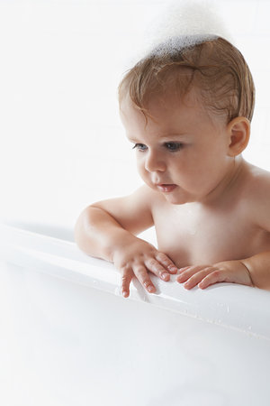 Hes having his bath before bed. An adorable baby boy standing in the bathtub.の写真素材