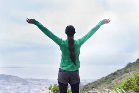 Ive reached the peak. Rearview of an adventurous young woman standing with her arms outstretched on the mountain.の写真素材