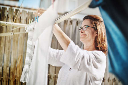 These will dry in no time. Shot of a mature woman hanging up laundry on a washing line outside.の写真素材