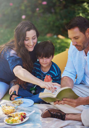 Their favourite story to read as a family. Shot of a parents reading a book to their son during a picnic in the park.の写真素材