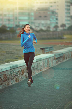 Running is a form of relaxation. Shot of a sporty young woman out running on the promenade.の写真素材