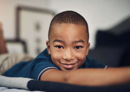 He has cute written all over him. Shot of an adorable little boy lying on his bed at home.の写真素材