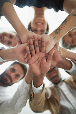 We do it together or not at all. Low angle portrait of a group of businesspeople putting their hands in a pile.の写真素材