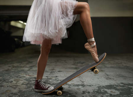 I have many talents. A cropped image of a woman on a skateboard wearing one sneakers and a ballet slipper.の写真素材