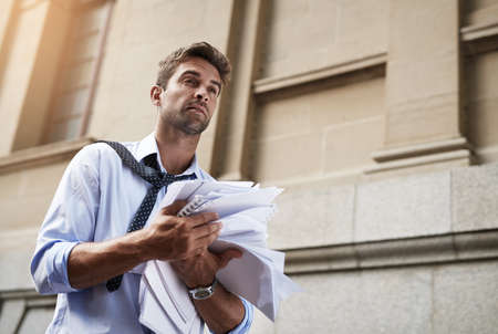 I need to put these in files. Shot of a stressed out young man holding a heap of paper documents...