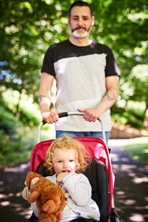 Strolling through the park. Portrait of a father pushing his little daughter in a stroller outdoors.