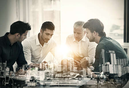 Knowing your business is the first step towards success. Cropped shot of a group of businessmen having a meeting around a table in an office superimposed over a city background.の写真素材