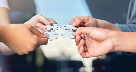 Lets put it all together. Closeup of businesspeople about to put four puzzle pieces together.