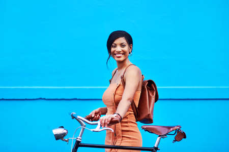 En route to happiness. Portrait of an attractive young woman traveling with her bicycle against a blue background.の写真素材
