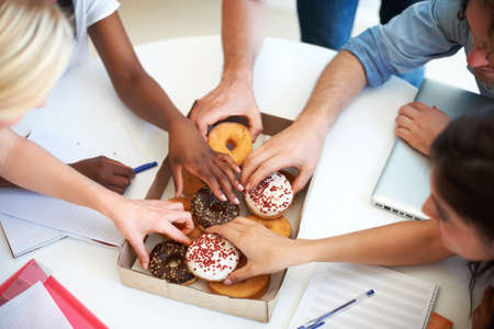 Energy for busy professionals. High angle shot of a group of businesspeople grabbing doughnuts while in a meeting.の写真素材
