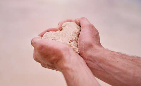 Summer is the season of love. Cropped shot of an unrecognizable man making a heart shape while holding sand on a beach.の写真素材